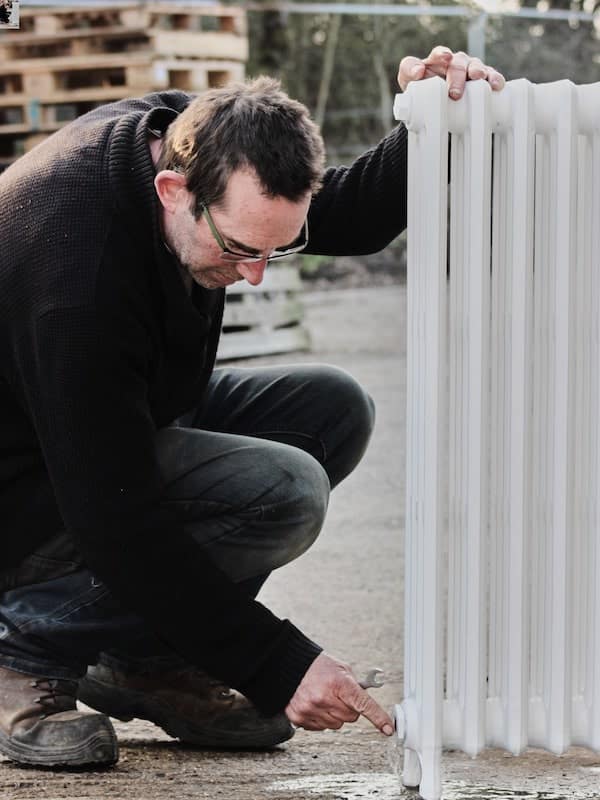 Person next to a primed cast iron radiator with a spanner draining water out of it
